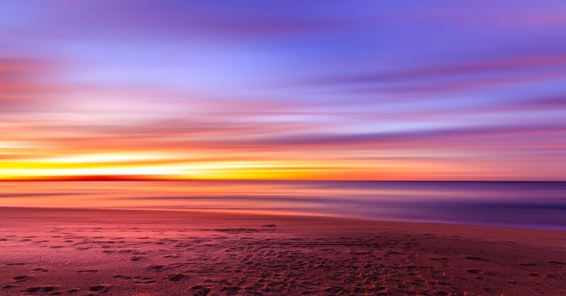 A colourful sunset at a beach looking out over the ocean.