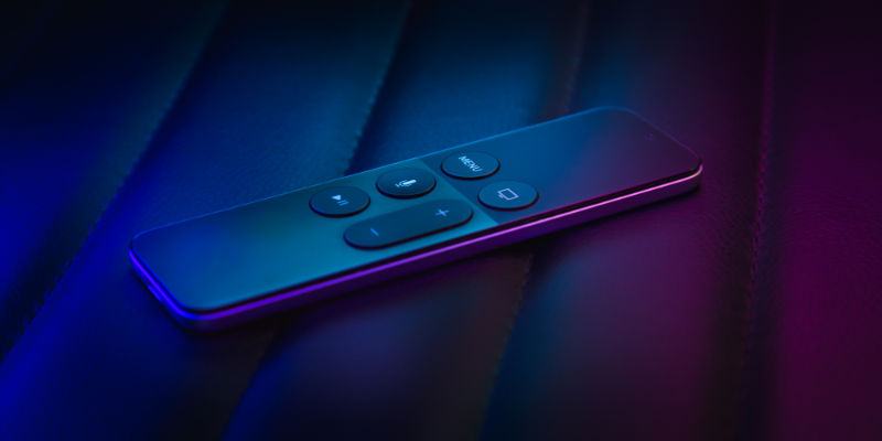 The Apple TV remote lit by blue and purple light.