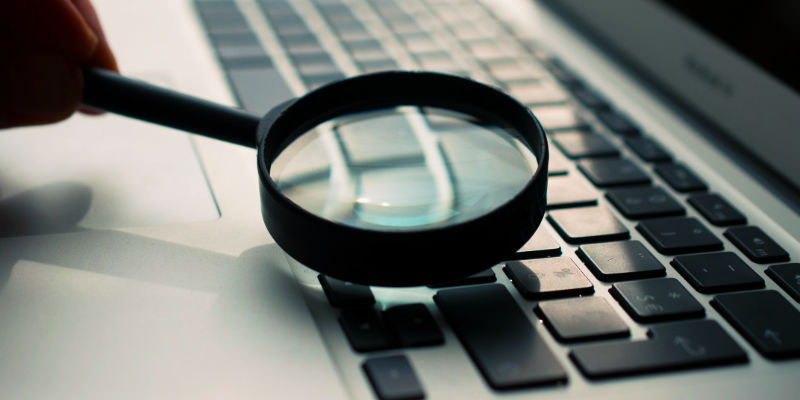 An open MacBook Air with a magnifying glass being swept over the keyboard.