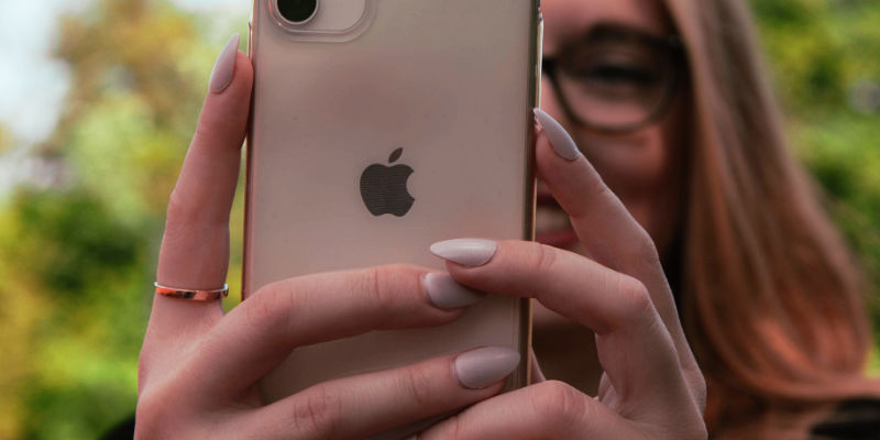 An iPhone sat on a wooden table. The iPhone simply displays the word Hello.