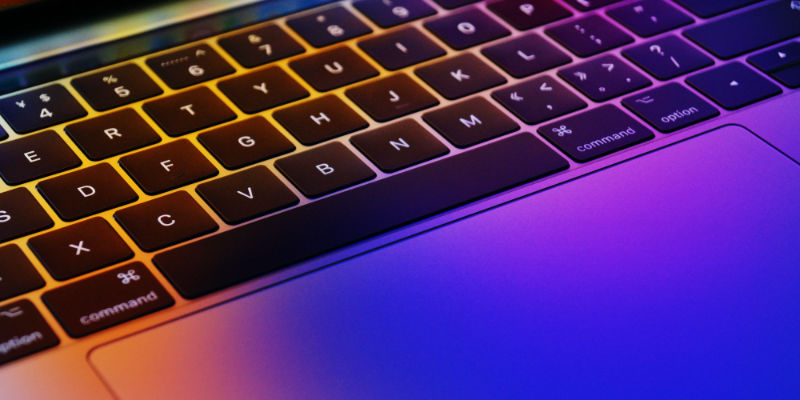 A close up of a MacBook Pro Keyboard coloured with purple and orange light.