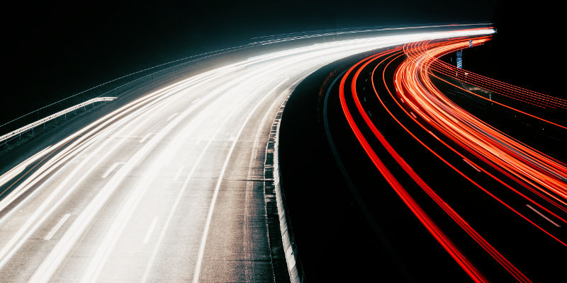 The rear wing of a car with the road streaking away behind it through a tunnel.