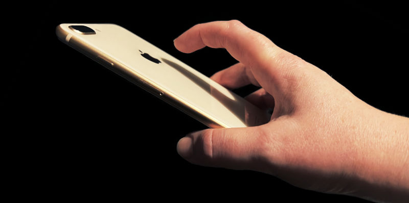 A hand with finger stretched to tap the back of a pink iPhone 8 Plus.